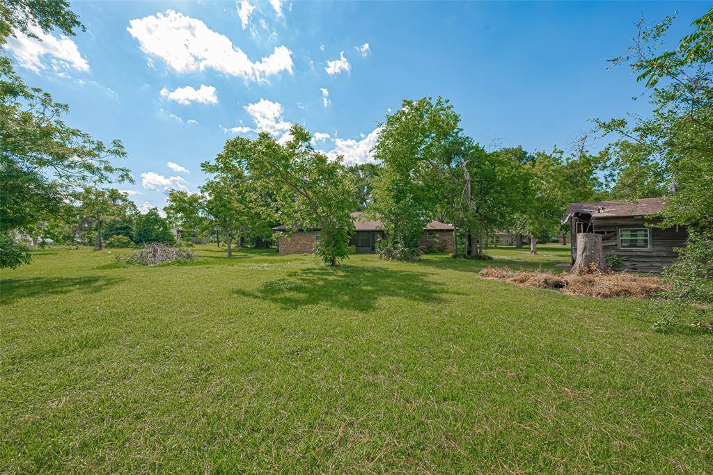 This photo showcases a spacious backyard with lush greenery, mature oak and pecan trees, and a charming rustic outbuilding. The main house features a screened porch, perfect for enjoying the outdoor space. Ideal for those seeking a serene and natural setting.