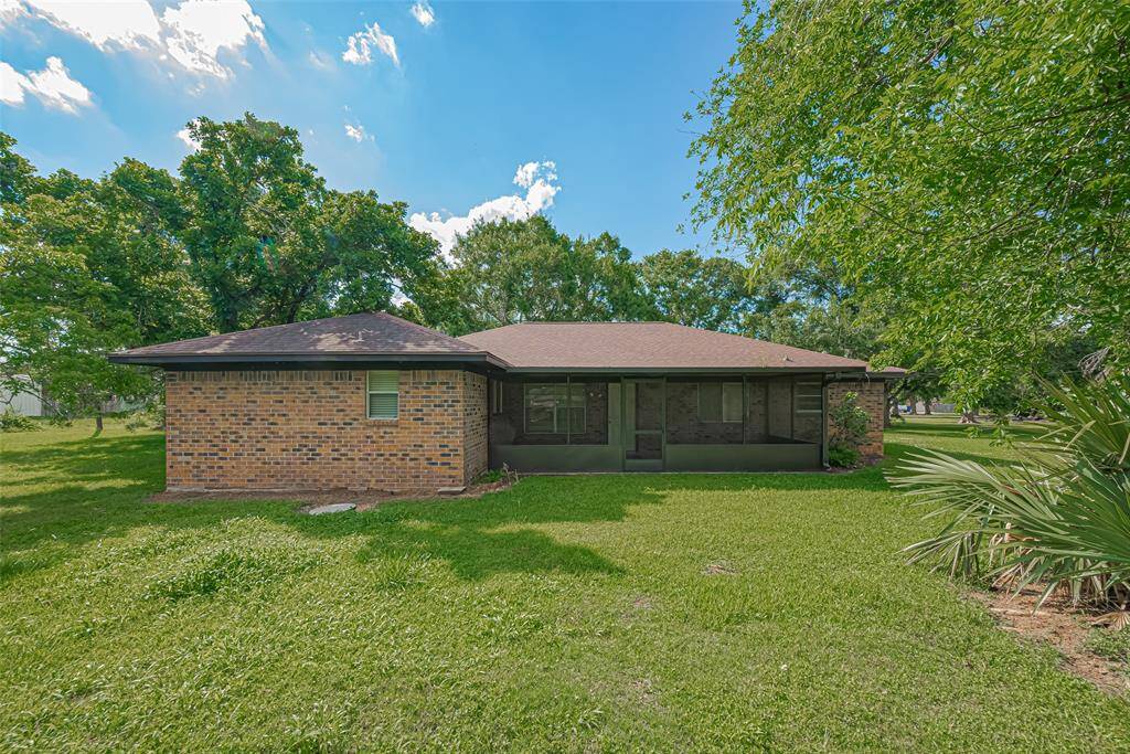Expansive, grassy property with mature trees and multiple rustic structures under a bright blue sky. Ideal for renovation or redevelopment.
