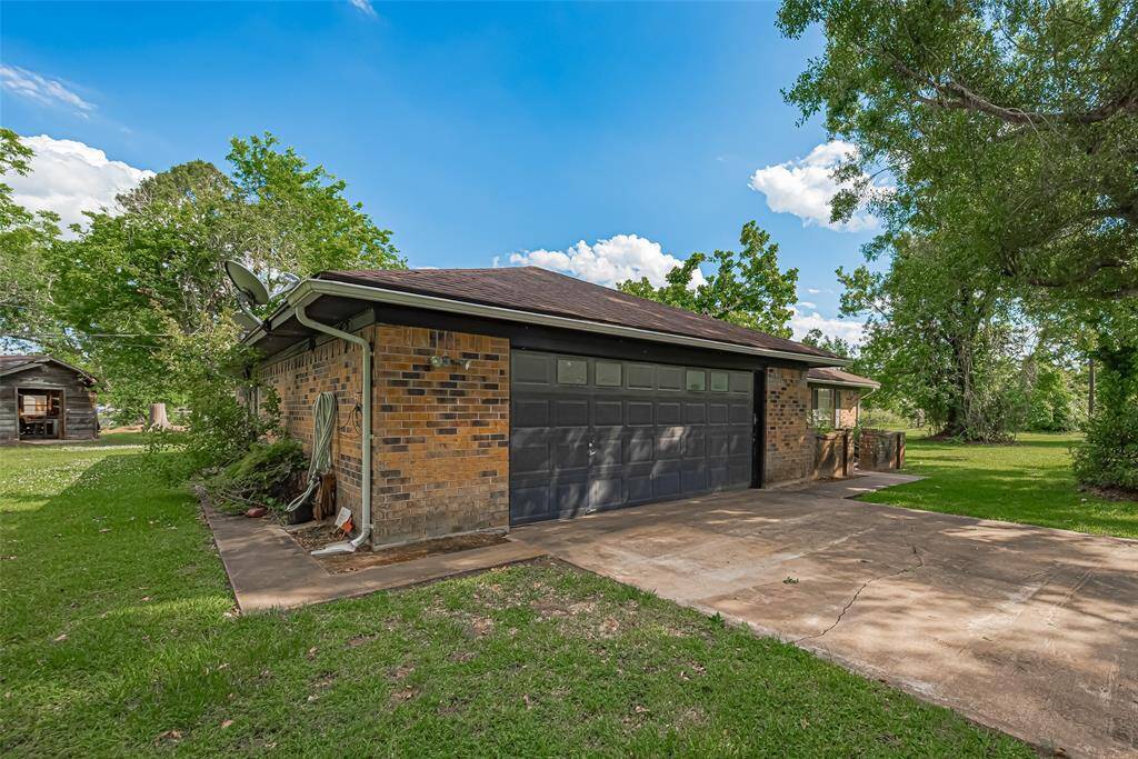 This charming single-story brick home features a classic design with a low-pitched roof and large front windows. It is surrounded by lush greenery and mature trees, offering a serene and private setting. The property includes a small front patio and a spacious lawn, ideal for outdoor activities.