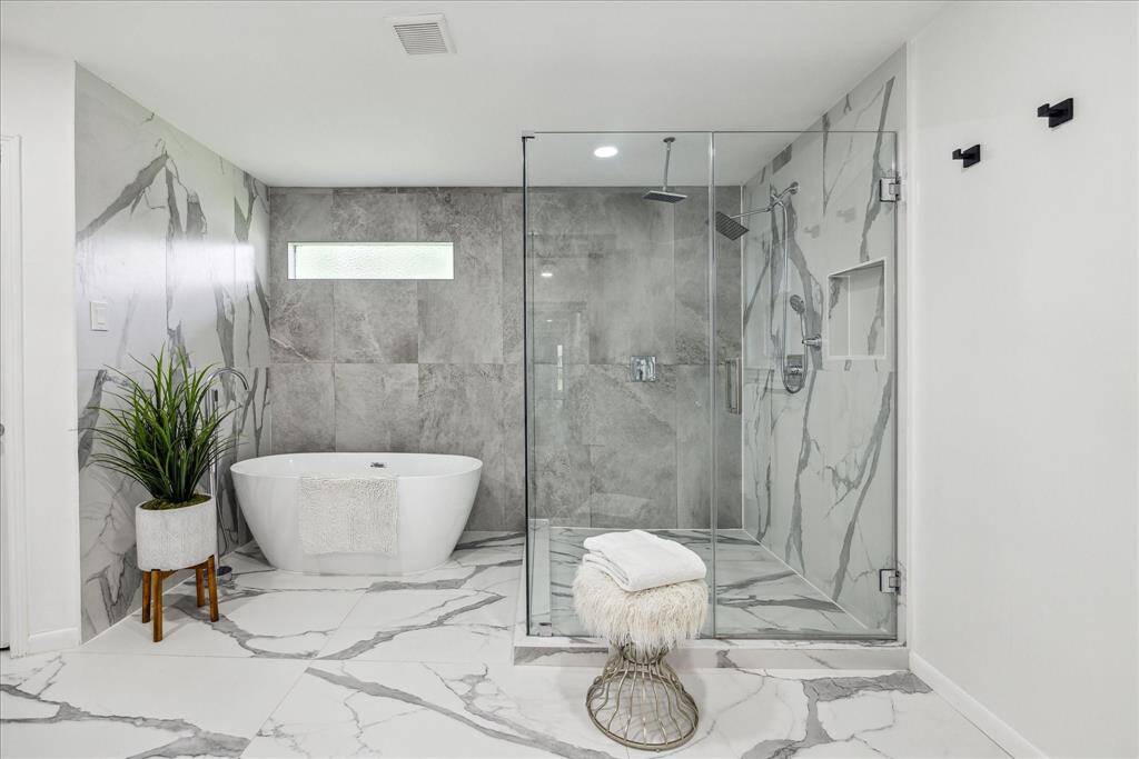 The primary en-suite bath features a standalone tub with a sleek chrome, floor-mounted faucet. This oversized frameless glass shower features modern tile, a rain head, and a handheld showerhead for a luxurious experience