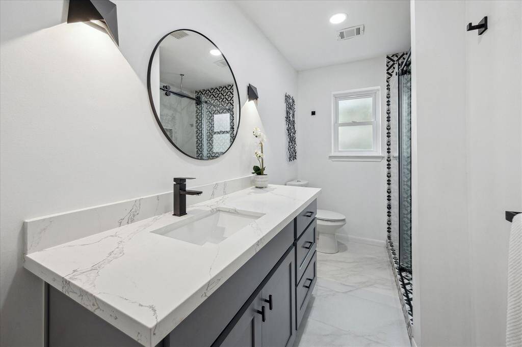 This stylish bathroom boasts a Shaker-style vanity, quartz countertops, and decorative lighting with a matching mirror