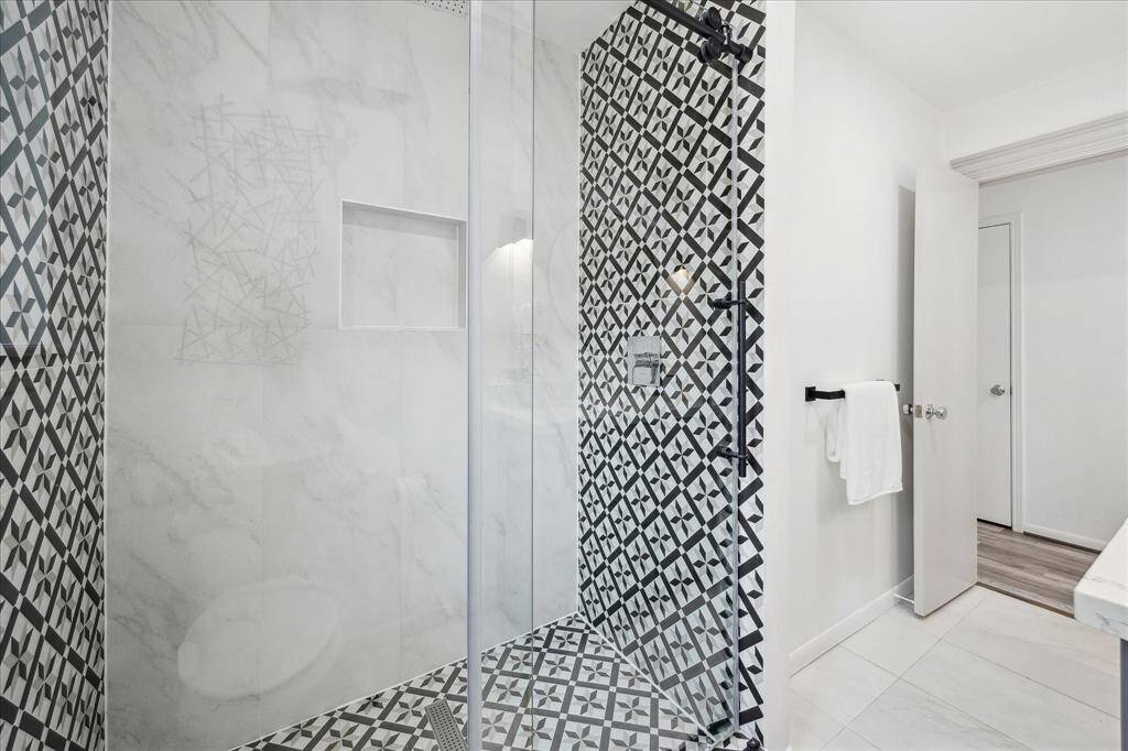This oversized shower features a shampoo nook, contemporary tile, and sleek glass doors