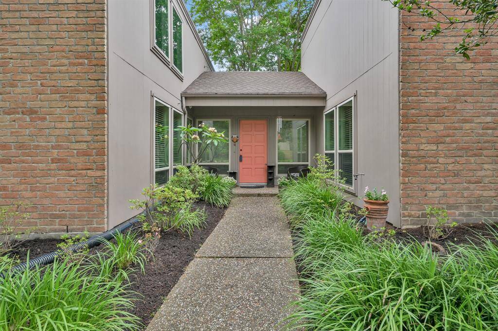 Step into this charming home featuring featuring a contemporary design with a brick exterior, set within a lush, landscaped yard. The inviting entrance is framed by mature trees and greenery, creating a serene and welcoming atmosphere.