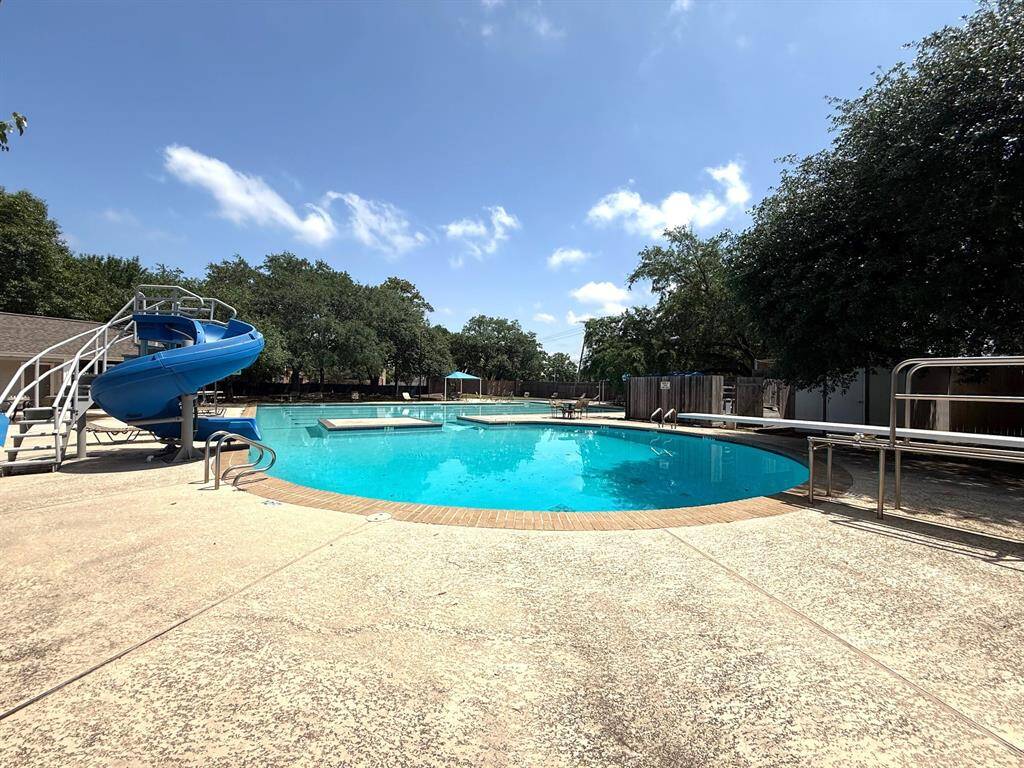 Spacious outdoor pool area with a fun blue slide, surrounded by lush trees, perfect for relaxation and family enjoyment.