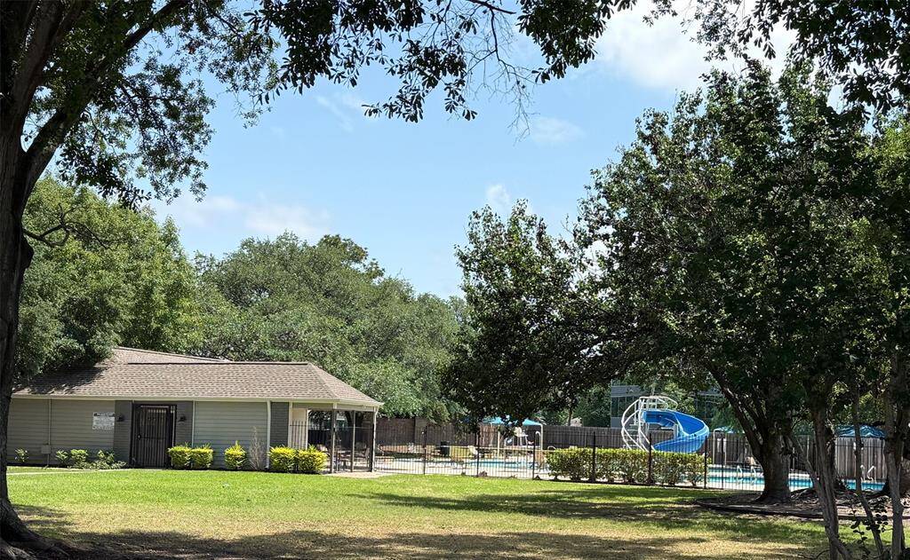 Community area with a swimming pool and slide, surrounded by trees and open grassy space, ideal for family recreation and relaxation.
