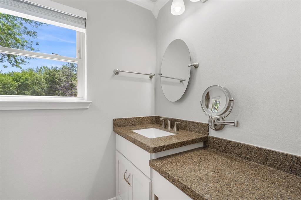 Primary bathroom vanity with granite and newer cabinets for storage.