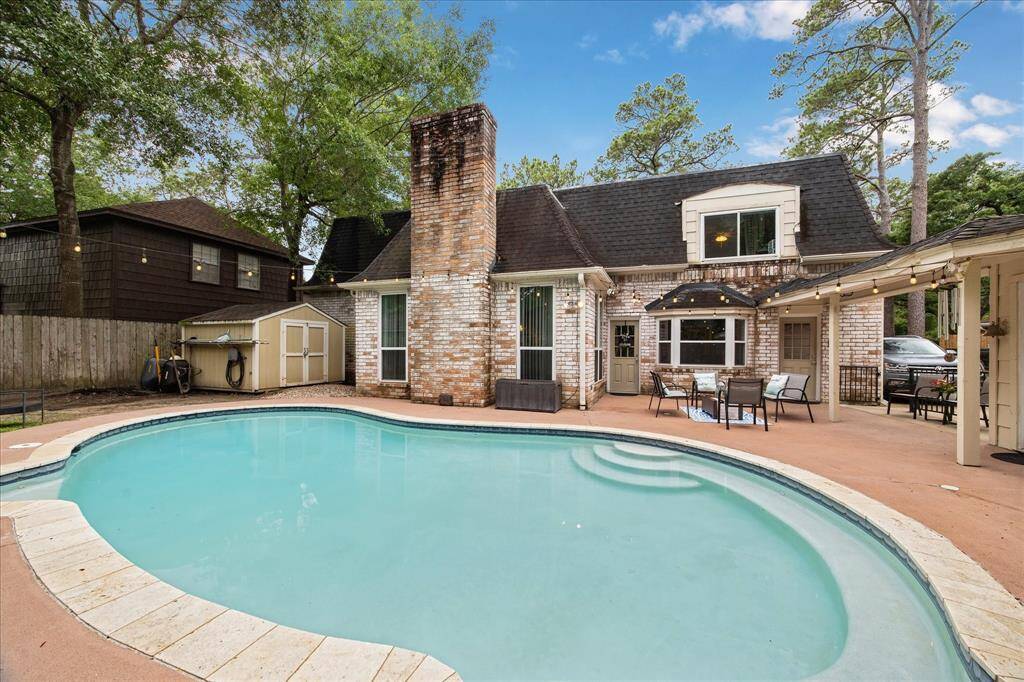 Charming backyard with a stylish pool, brick exterior, and cozy patio area perfect for relaxation and entertaining. Surrounded by mature trees for added privacy.