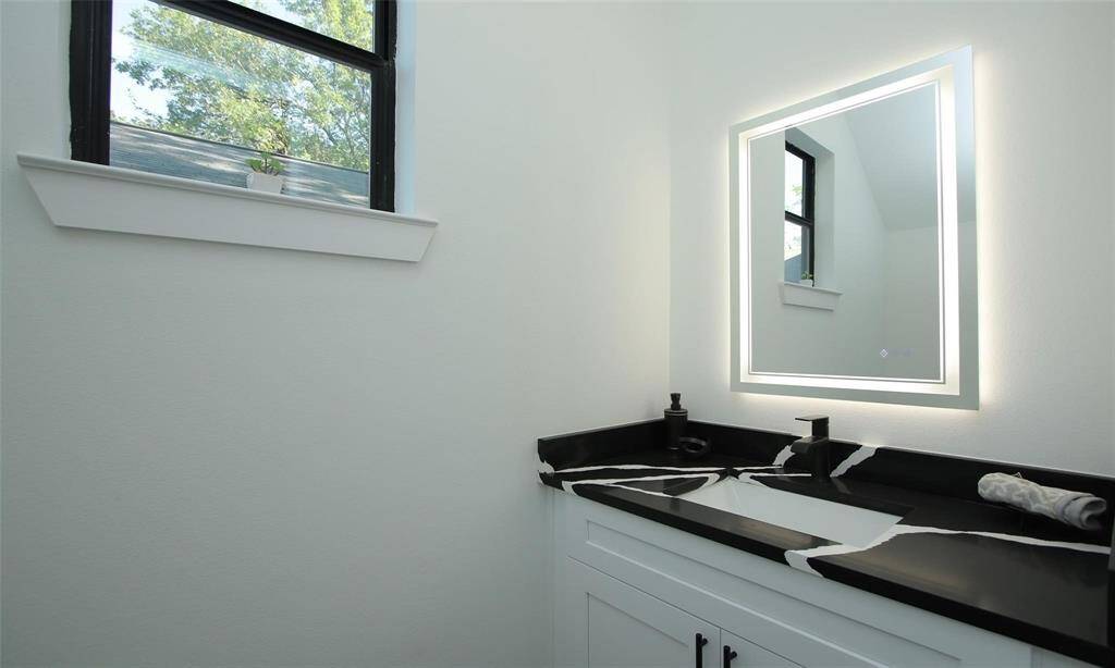 This first floor primary bedroom features hardwood flooring and a modern ceiling fan, with ample natural light from large windows and sliding glass doors leading to a covered back patio. It includes a walk-in closet.