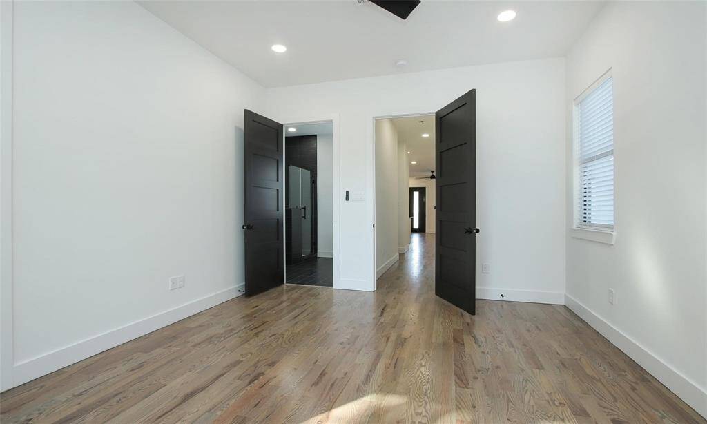 This primary bathroom features oversized black tiles, a spacious glass enclosed custom shower, a freestanding white tub, and a stylish dual-sink vanity with illuminated mirrors.