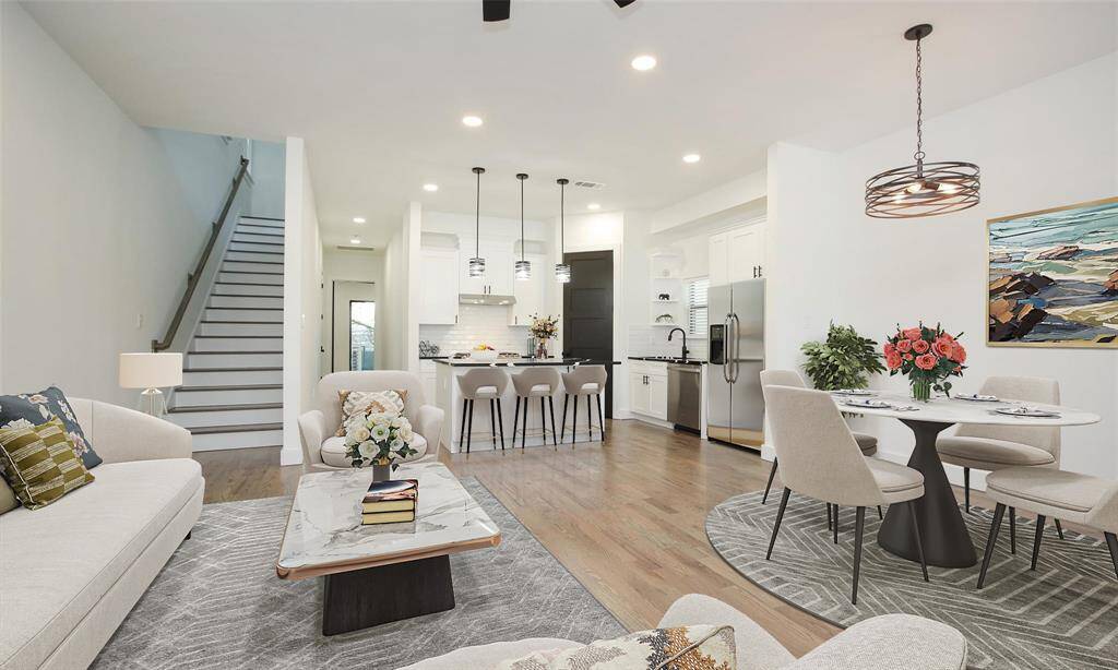 This photo showcases a modern, open-concept living space with hardwood floors, a stylish kitchen with an island and pendant lighting, and a staircase leading to the upper floor. The space is bright with recessed lighting and a contemporary chandelier, offering a clean and inviting atmosphere.