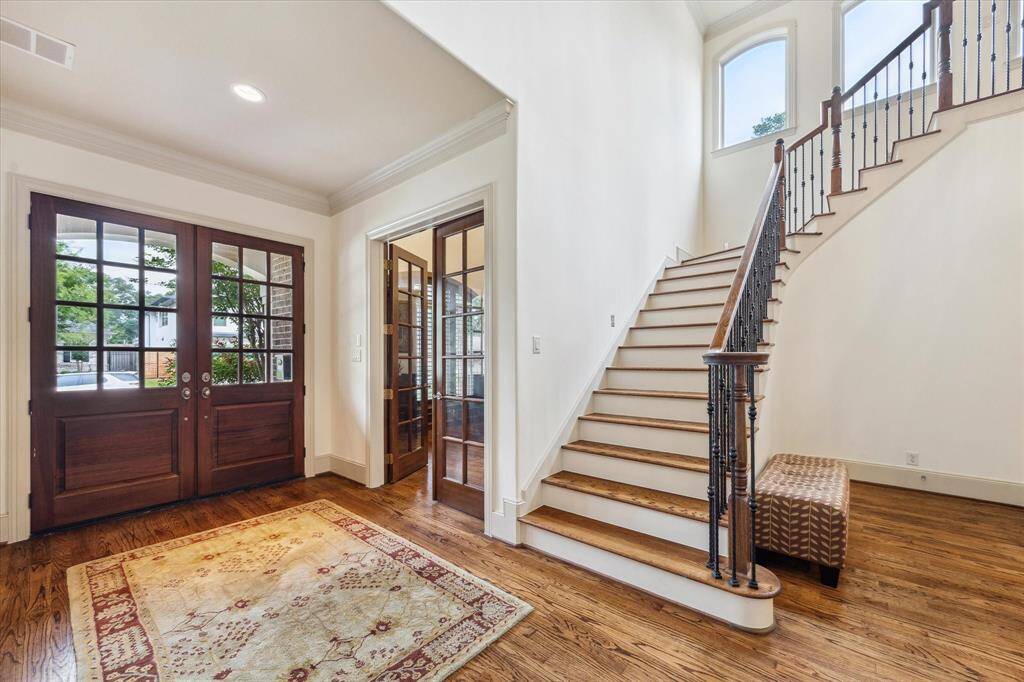 The home features rich hardwood floors, with elegant French doors opening to a private study, and a staircase adorned with wrought iron railings leading to the upper level.