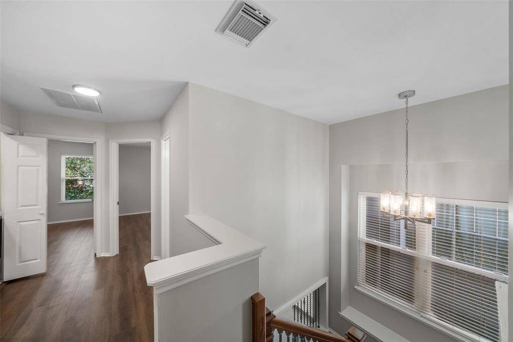 A striking view of the second-floor hallway, featuring new engineered wood floors, and a view showcasing the foyer’s elegant light fixture.