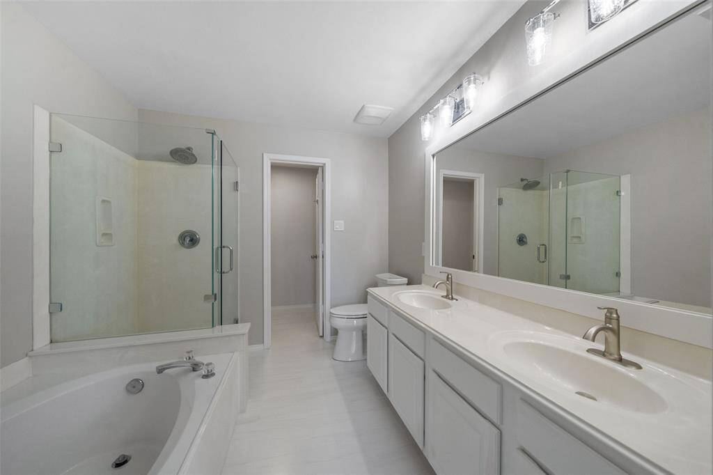 A stunning view of the primary bathroom, featuring new tile floors, a luxurious garden tub, a separate frameless shower, double vanities, and a spacious walk-in closet, providing both comfort and functionality.