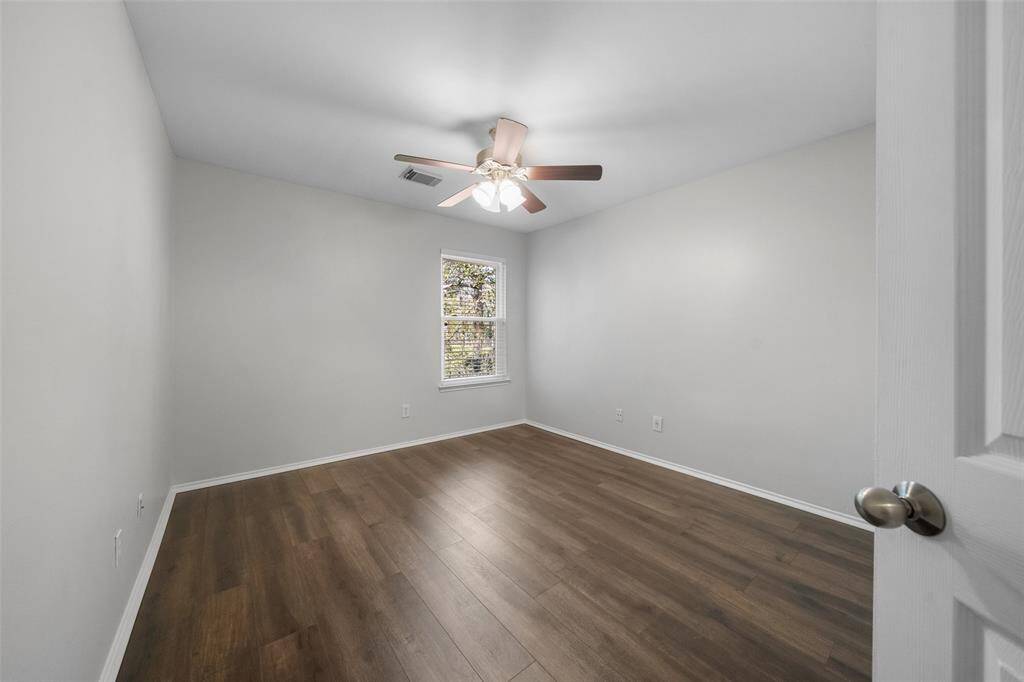 One of the two secondary bedrooms features new engineered wood floors, a ceiling fan, and a peaceful view of the back of the property, providing a serene and comfortable space.