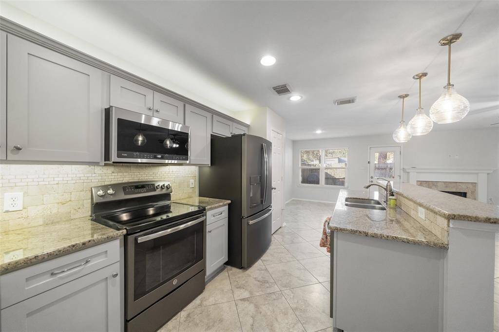 Take in the stunning view of the kitchen, featuring elegant granite countertops, light and bright cabinets, a sleek electric stainless steel stove, a large refrigerator, and a built-in microwave for a perfect blend of style and functionality.