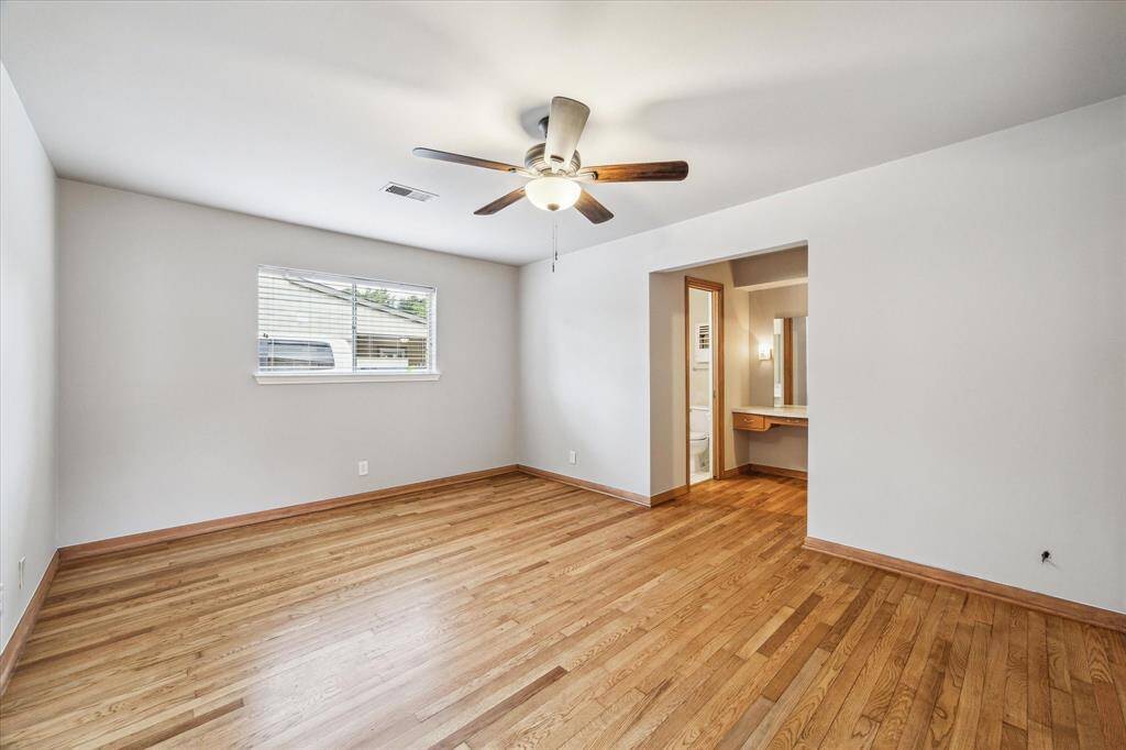 Primary bedroom with hardwood floors, ceiling fan and door (not pictured) that leads to the covered patio.