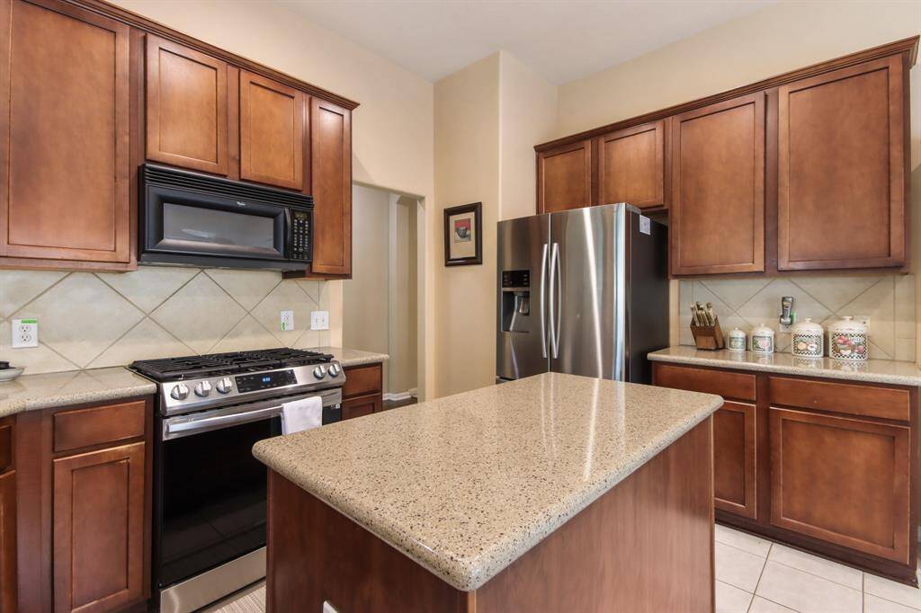 This modern kitchen features dark wood cabinetry, a sleek stainless steel refrigerator, and a gas stove with a built-in microwave. The spacious island and tiled backsplash offer a stylish and functional space.