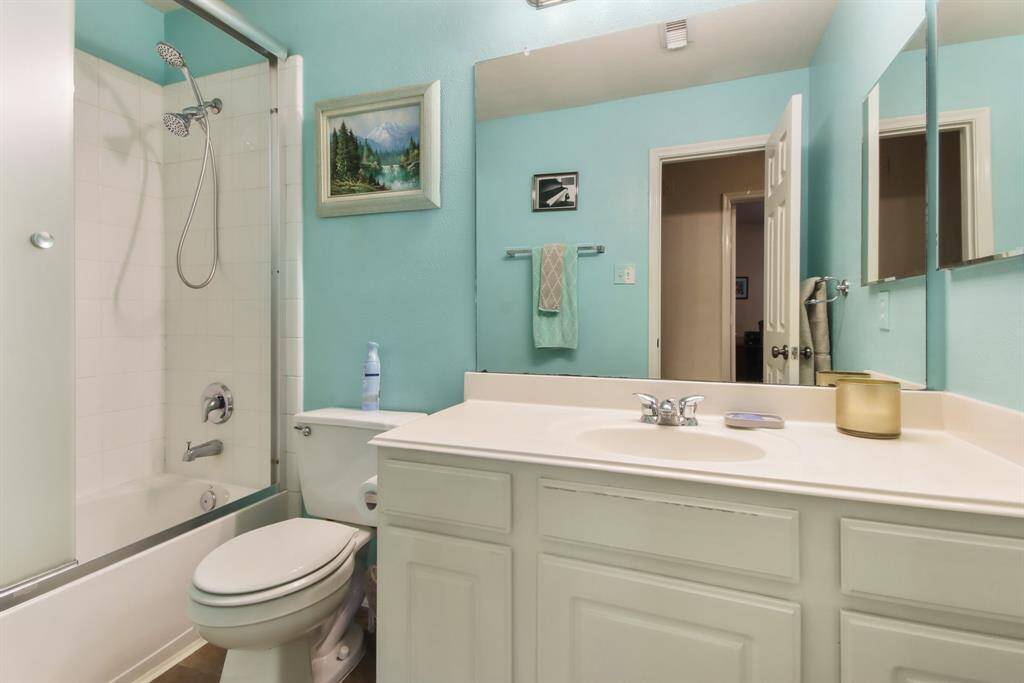 This bathroom features a clean and bright design with teal walls, a white vanity, and a shower-tub combo with sliding glass doors. It includes a large mirror, modern fixtures, and some decorative touches for a welcoming feel.