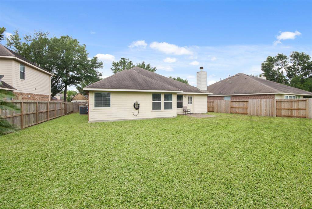 This photo shows a spacious backyard with well-maintained grass, a single-story house featuring a sloped roof and a chimney. It's fenced for privacy, making it ideal for outdoor activities.