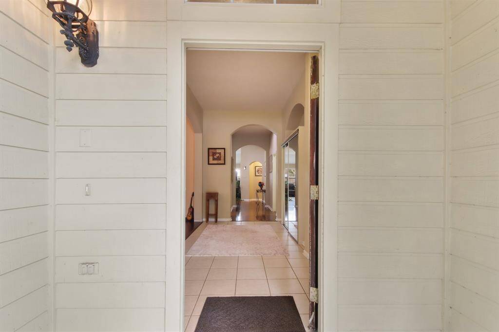 Welcome to a charming entryway featuring a tiled floor and neutral wall tones. The inviting hallway leads to an archway, offering a glimpse into the home's interior, with subtle decorative touches and warm lighting.