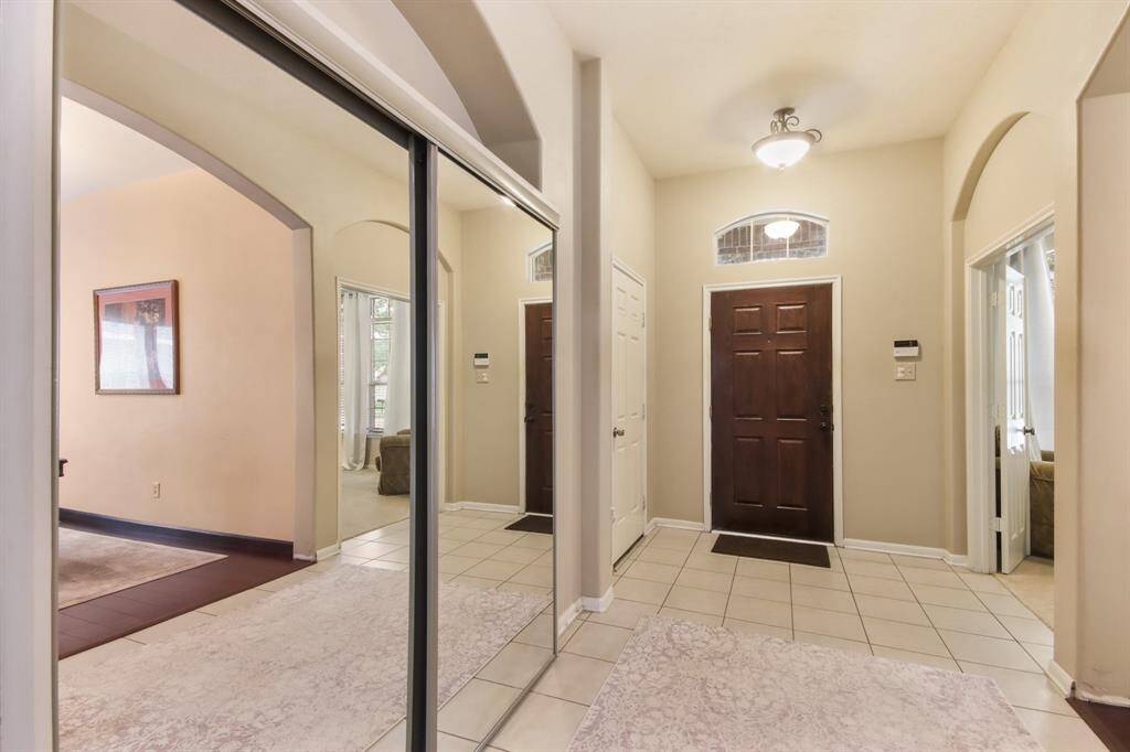 This entryway features a warmly lit space with a dark wood front door, tiled flooring, and mirrored sliding closet doors. Archways lead to adjacent rooms, providing an open and inviting atmosphere.