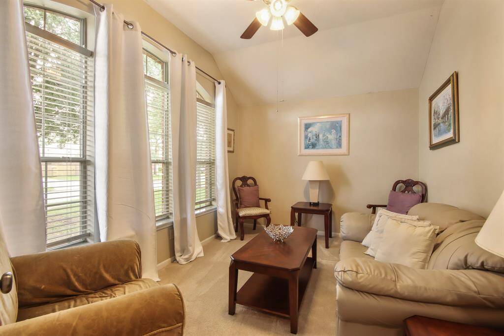Cozy formal living or home office with soft beige walls and carpet, large windows with white curtains to provide natural light.