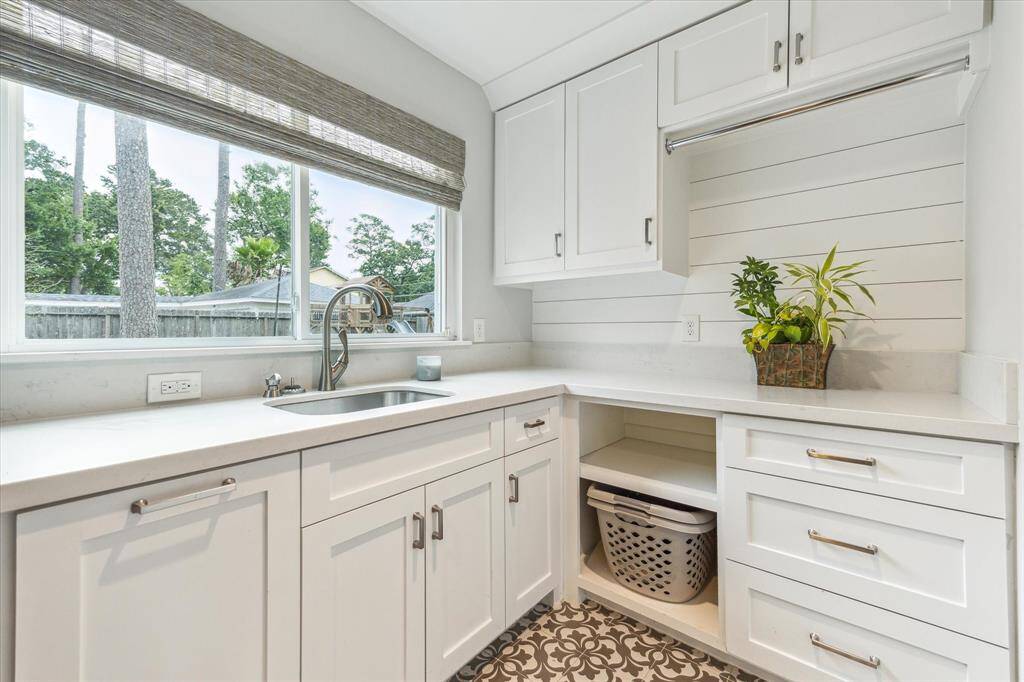 Custom laundry room with a view of the backyard is beautifully designed with designer flooring, custom cabinetry, bar for hanging laundry, and an undermount sink!