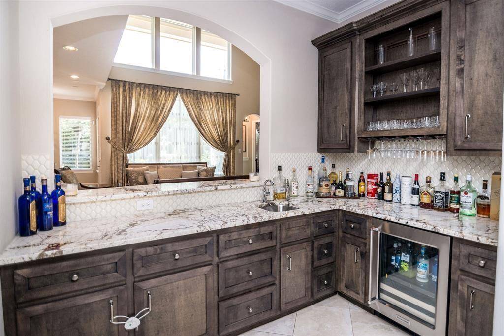 Elegant and inviting bar area featuring custom cabinetry, a sleek marble countertop, and a built-in wine fridge, perfect for entertaining.