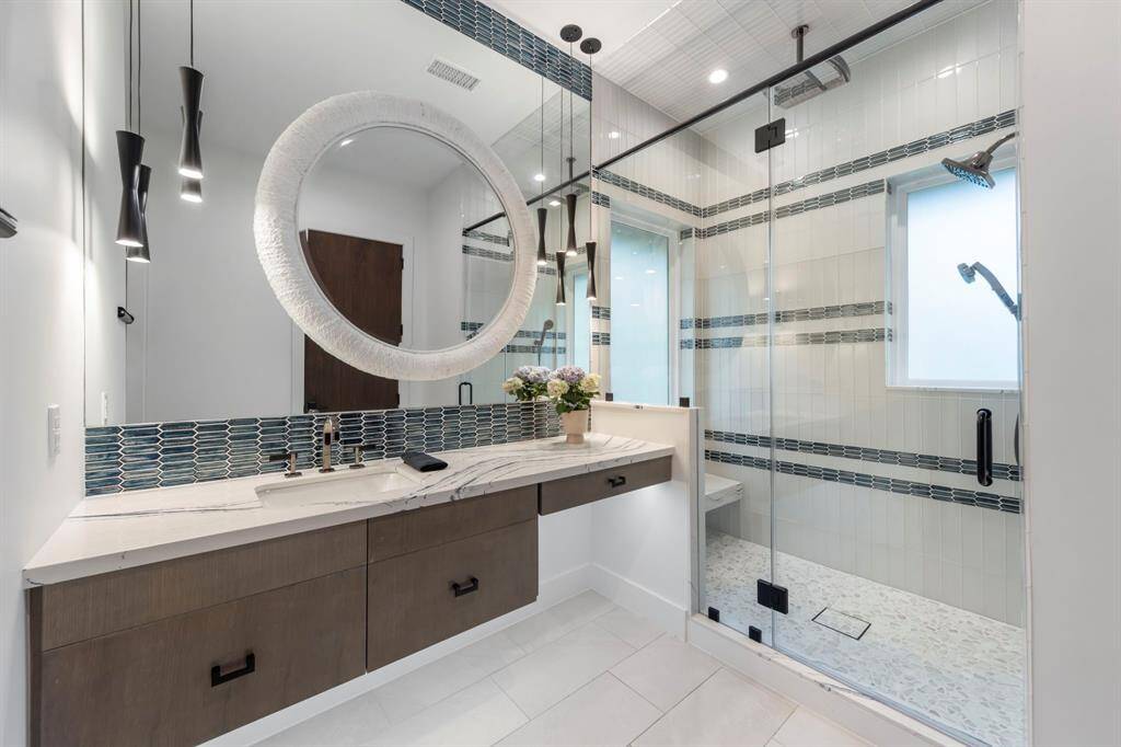 En-suite contemporary bathroom features a sleek vanity and a spacious glass-enclosed shower accented with modern tile patterns and dual showerheads.
