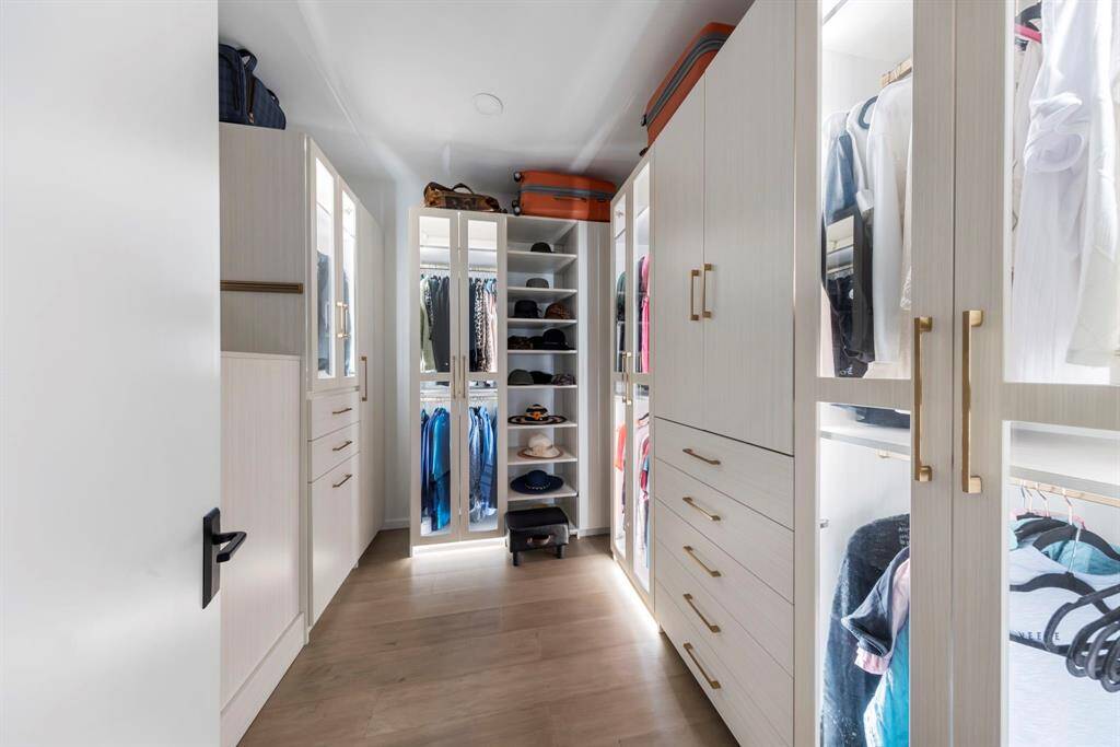 This walk-in closet features custom light wood cabinetry with glass-front doors, integrated lighting, brass hardware, and optimized storage for a sleek, functional, and cohesive design.