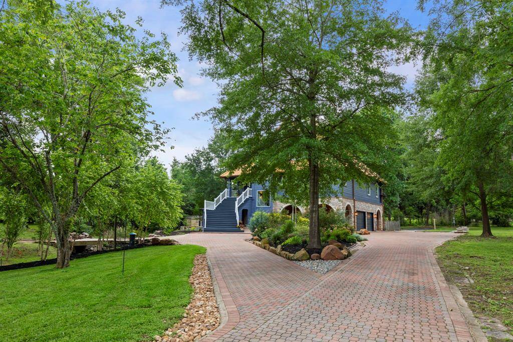 Nestled in lush landscaping, a blue-and-stone home awaits at the end of a winding stone driveway.