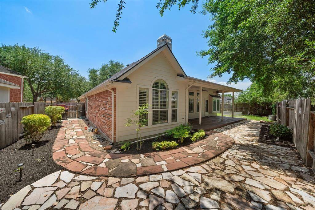 Professionally landscaped backyard with flagstone extension and pathway. A sidewalk from the driveway to a concrete pad for garbage can storage is just inside the back fence. Covered back patio with ceiling fans. Such a peaceful backyard!