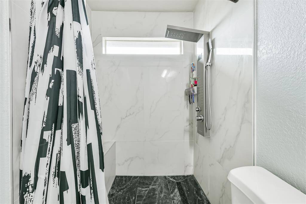 The primary bath features a stunning walk-in shower with marble-look tile, a sleek rain shower panel, and a modern horizontal window for natural light and privacy. It’s a spa-inspired upgrade that adds a touch of luxury to your daily routine.