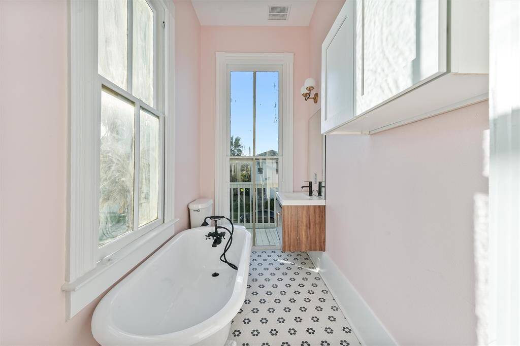 Bright and airy bathroom with soft pink walls, patterned tile floors, and French-style windows that open to a Juliet balcony.