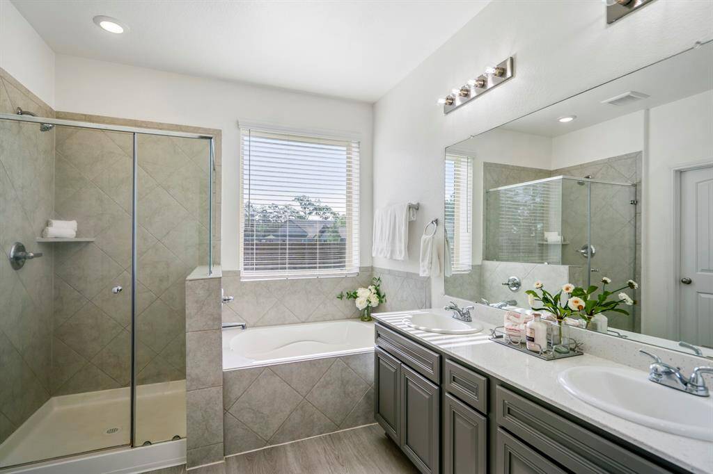 The primary bath features dual sinks, a soaking tub with a window above, and a separate tile shower with a sleek glass frame, offering both style and functionality.