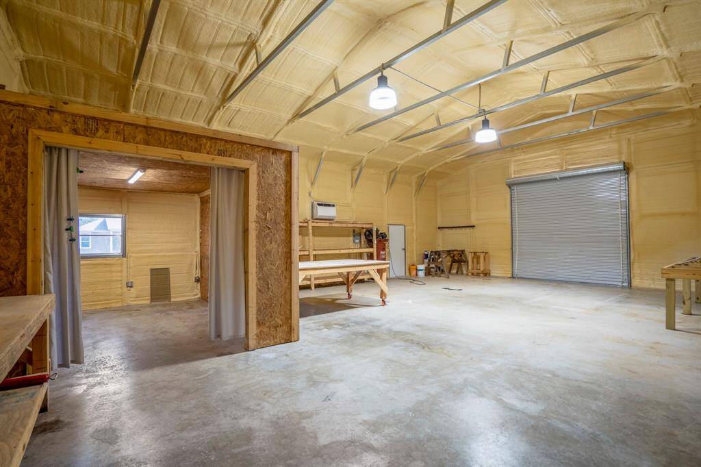 Another view inside the building reveals a small room thoughtfully built into the open space, offering a private area for storage or work. Beyond, the large roll-up door along the side wall provides easy access for larger items or equipment.