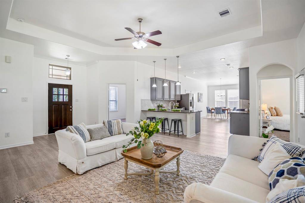 As we move toward the back of the living room and turn to look back, the kitchen comes into full view with the dining area just beyond. To the left, the flexible front room offers space for a study or guest room, while an arched doorway to the right leads to the private primary suite.