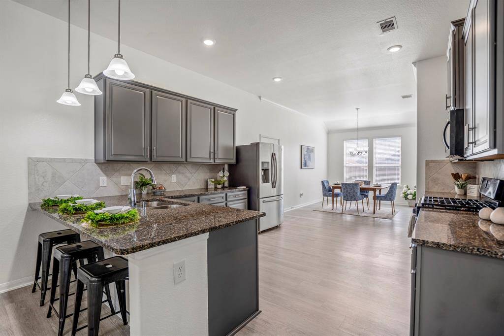 As we step into the kitchen, the functional layout becomes clear, with the kitchen positioned between the living and dining areas. The breakfast bar backs to the living room, creating a seamless flow. Grey cabinetry with modern hardware, paired with sleek granite counters, adds both style and practicality to the space.