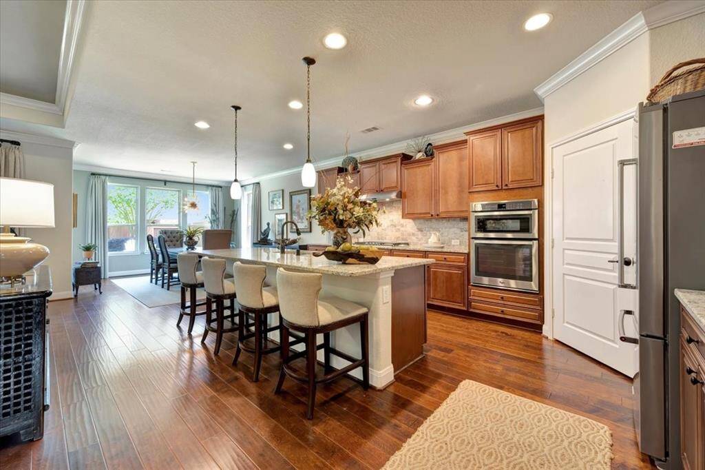 Gourmet kitchen seamlessly opens to the dining and living areas, featuring rich wood cabinetry, granite countertops, a large center island with breakfast bar seating.