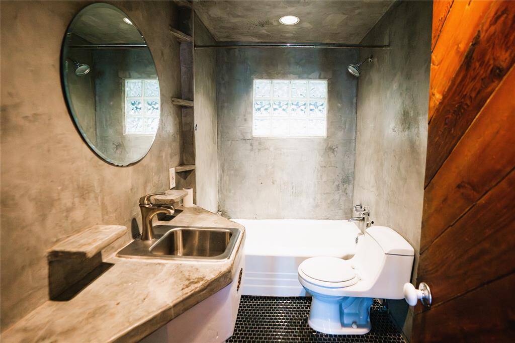 Beautiful secondary bathroom has modern cement accents, tile flooring and cedar door.