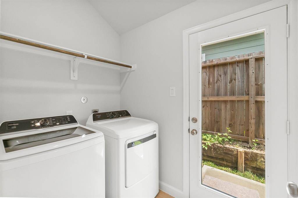 Bright and functional laundry room featuring a washer, dryer, storage shelf, and a glass door opening to the backyard.