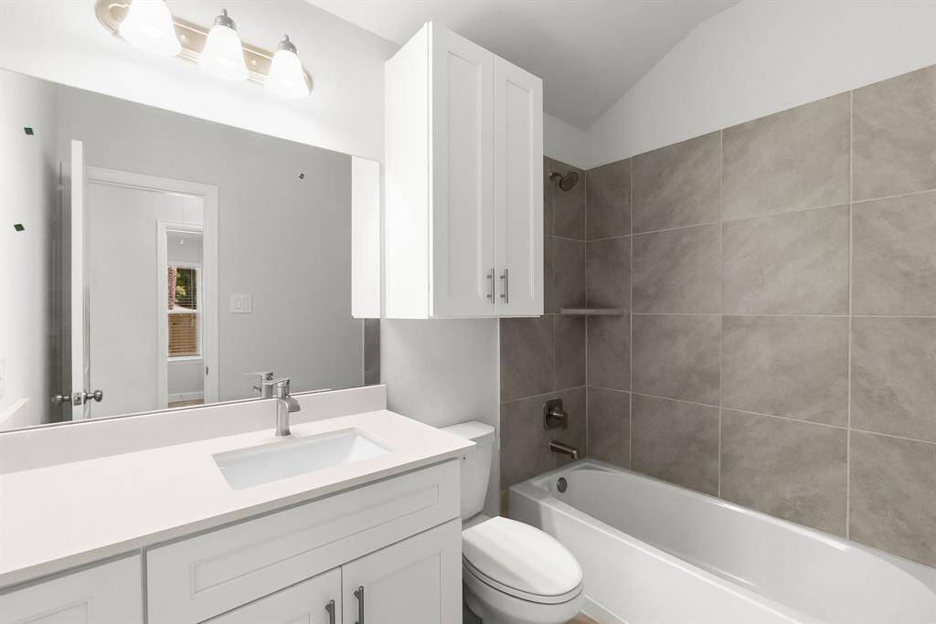 Experience modern elegance in this bathroom, featuring neutral tones, a sleek white vanity with ample storage, a large mirror, and a stylish bathtub with a tiled shower. Bright lighting and contemporary fixtures create a clean, inviting atmosphere.