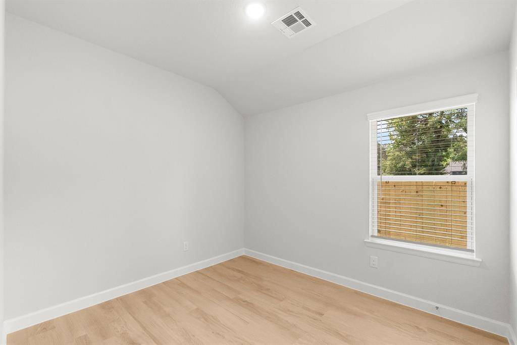 Bright room with light wood flooring and neutral walls, featuring a window overlooking a fenced yard and trees. Recessed ceiling light. Perfect for a bedroom or office.