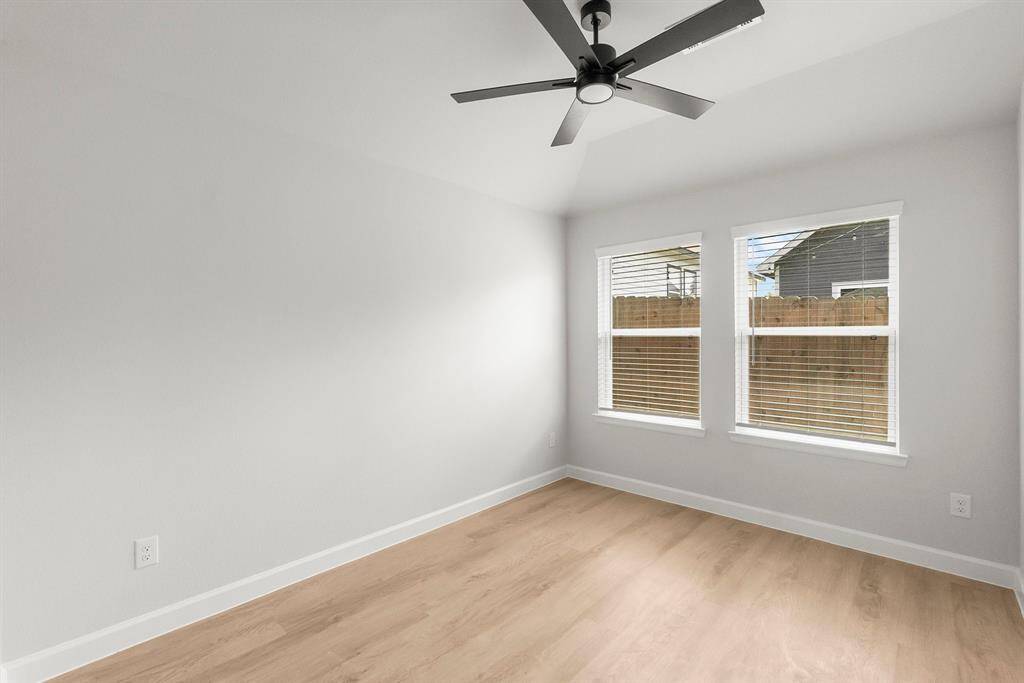 Bright, minimalist room with light wood flooring, two large windows, and a modern ceiling fan. Ideal for a cozy bedroom or office space.