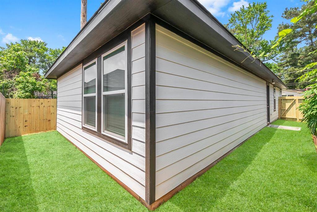 This photo shows the side of a house with light-colored siding and two large windows. It features a well-maintained lawn and a wooden fence, providing a private outdoor space.