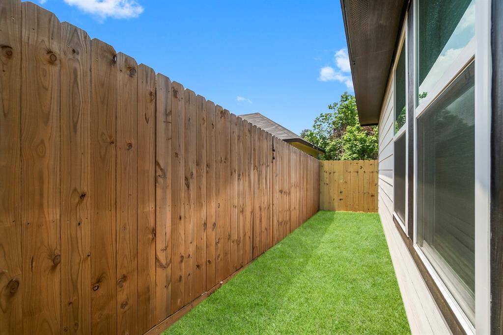 This photo shows a narrow side yard with a wooden privacy fence and well-maintained grass, adjacent to the house. The area is bright and sunny, offering a cozy outdoor space.