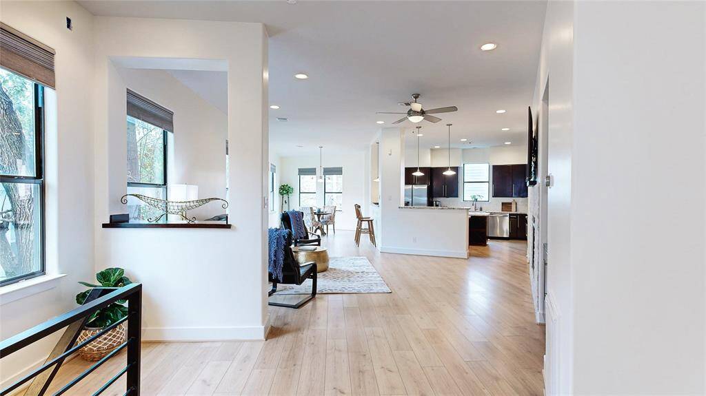 This open-concept living space features light wood-look flooring, a modern kitchen with dark cabinetry, and a breakfast bar. The room is bright with natural light from multiple windows, and it has a cozy living area with a fireplace and built-in shelving. Stylish and inviting, perfect for entertaining.