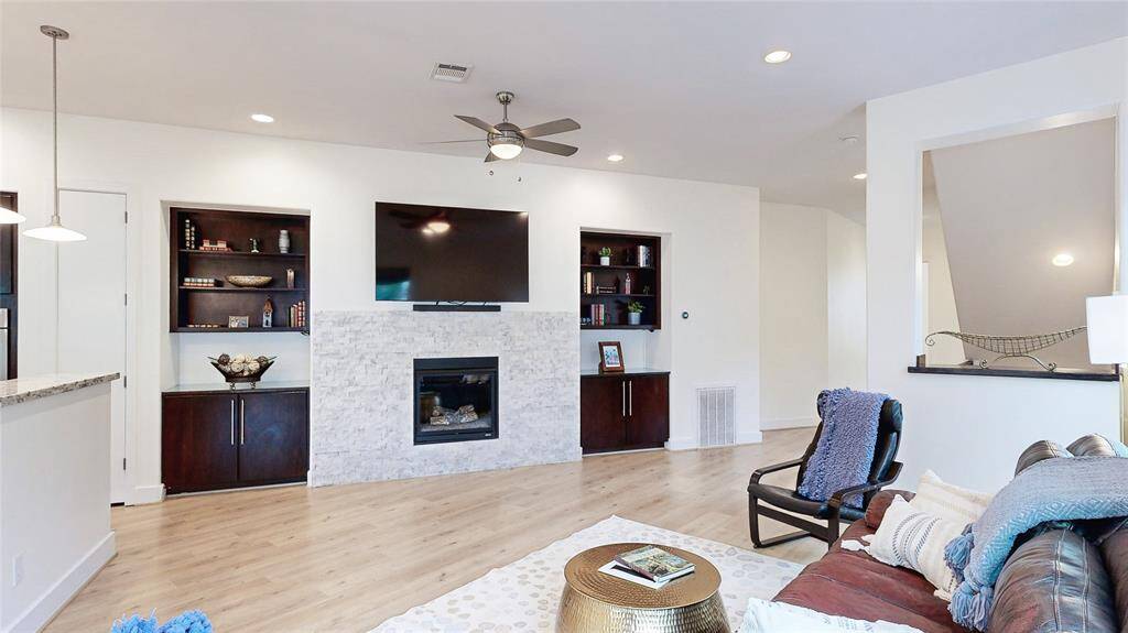 This photo showcases a modern living room with a sleek electric fireplace framed by white stone. Built-in dark wood shelves and cabinets provide stylish storage, creating a cozy and functional space.