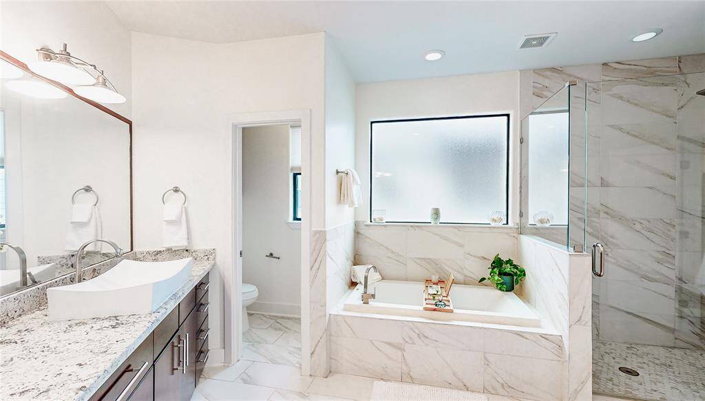 This bathroom features a modern design with granite countertop, dual vessel sinks, and elegant cabinetry. It includes a spacious walk-in shower and a separate jetted bathtub, complemented by large frosted windows for natural light and privacy.