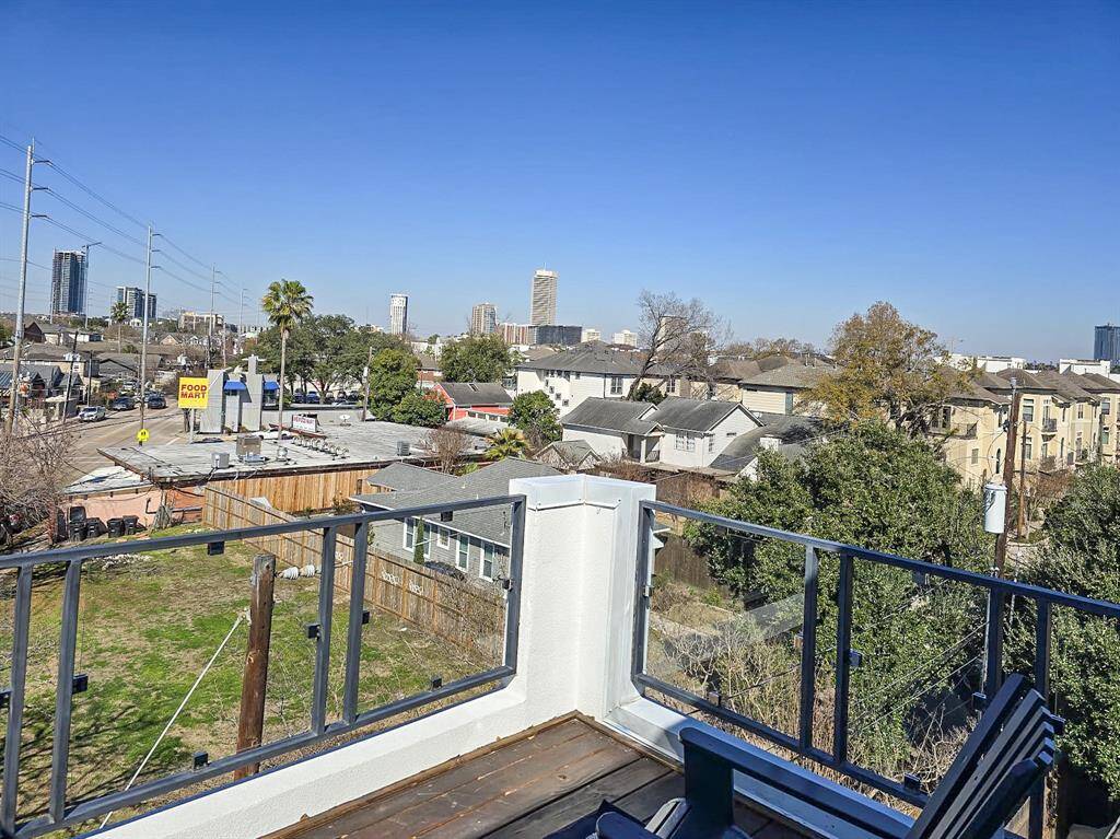 Rooftop deck with modern glass railing, offering expansive views of the city skyline and surrounding neighborhood. Ideal for relaxation and entertaining.